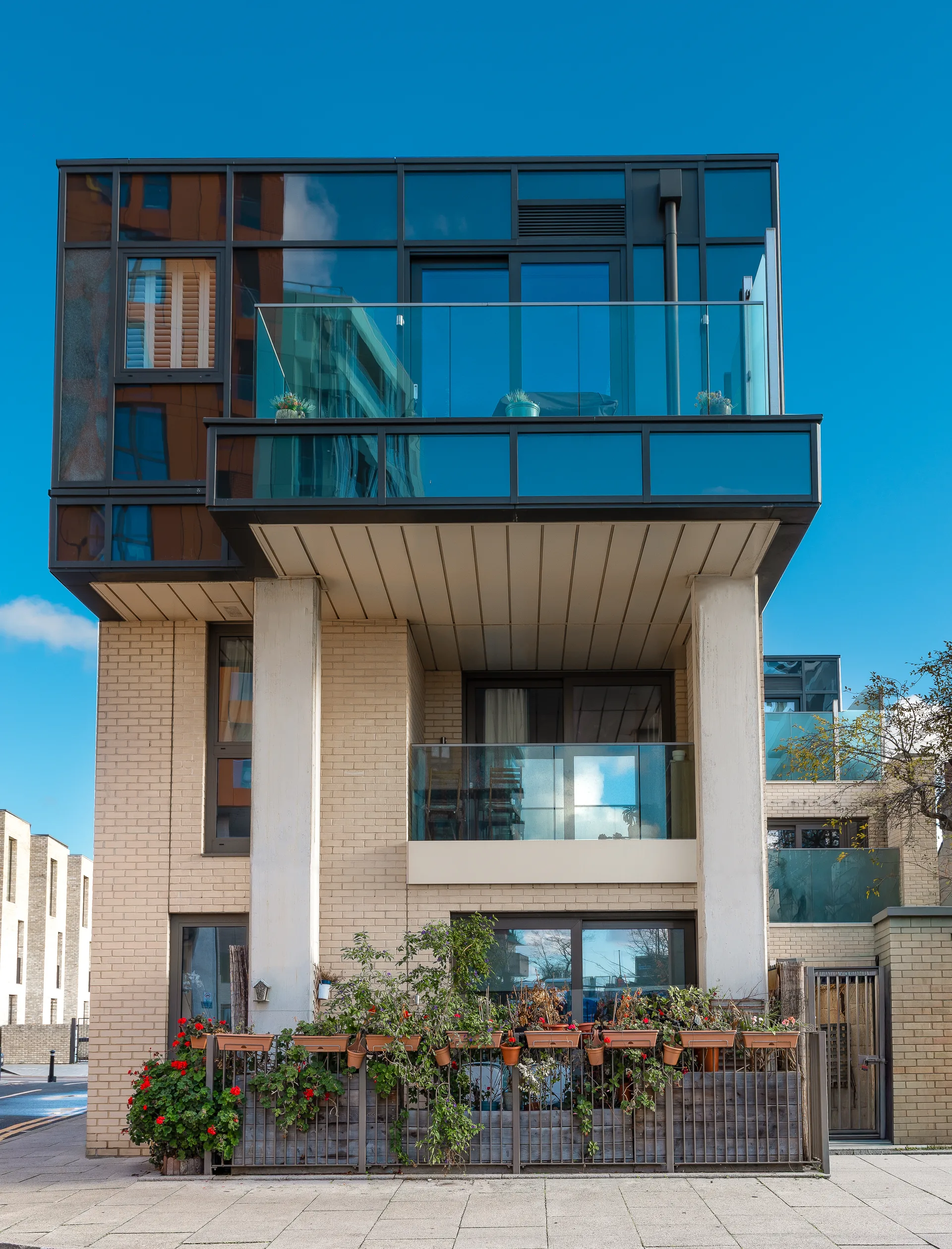 Modern Multi Story Apartment Building With Large Glass Balconies And Tan Brickwork Under A Clear Blue Sky.